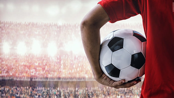 A soccer player holding a soccer ball under his arm in a packed stadium