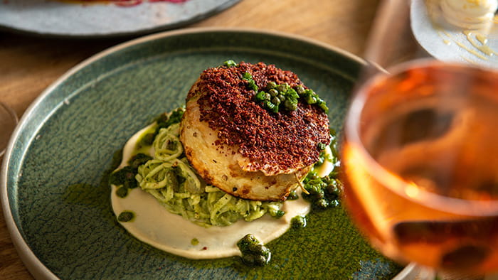 A fine dining dish with a crab cake on a bed of pasta with pesto and a white puree