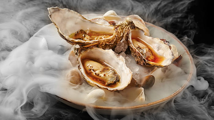 A fine dining dish of oysters on sea shells with dry ice smoke.