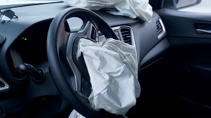 A car's steering wheel with a deployed and damaged airbag