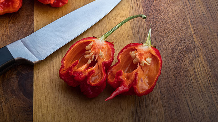 A vibrant red Carolina Reaper pepper with its unique stinger tail, placed amidst other peppers.