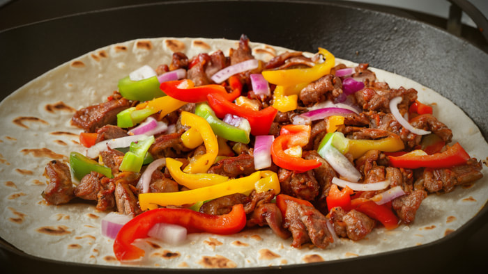 A sizzling skillet of fajitas with strips of grilled meat, colorful bell peppers, and onions, ready to be wrapped in a warm tortilla.