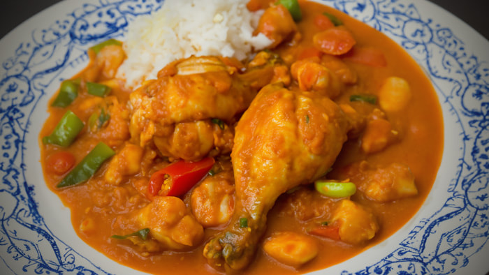 A spicy bowl of Vindaloo, rich in color and garnished with fresh herbs, served with a side of rice.